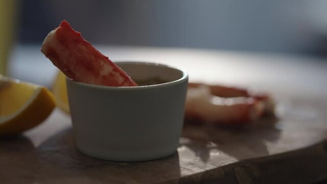 Slow motion gimbal shot of crab leg meat on a olive board with sweet lemon and dip sauce on concrete countertop