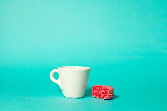 White cup of espresso with bitten macaroon cookies on a blue background.