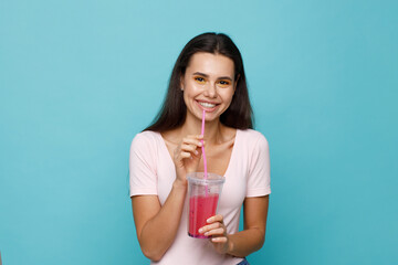 Young girl drinking fresh juice from plastic cup take-out food. Woman with berry lemonade on blue background. Summer cold drinks.