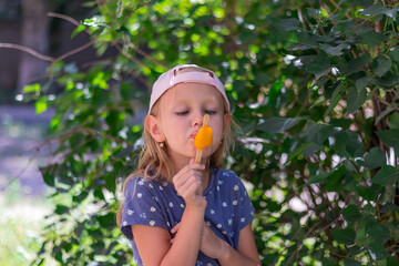 little girl, blonde, preschool girl stands in the park and eats popsicles