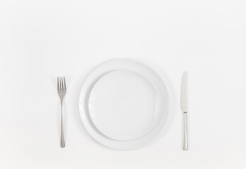 White table setting. Empty plate and silver cutlery on a white background. Copy space, top view, flat lay.