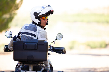 Vista trasera de viajero en moto con el casco abierto sobre fondo difuminado en tonos claros. Viajar en motocicleta.