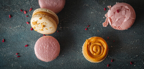 Flat lay of yellow and pink macaroons on the dark concrete background. Macro shot of cracked French sweet dessert cookies with crumbs