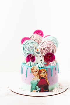 Kyiv, Ukraine - March 03, 2021: Disney character Elsa with sister Anna and her friend Olaf snowman cookies on the top of birthday cake. Frozen cartoon characters. White background