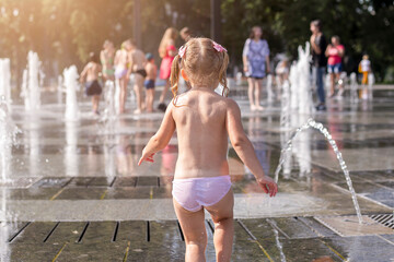 Cute little girl playing on urban jet fountains with splashing water