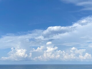 Naklejka na ściany i meble Sky clouds over sea water. Heaven clouds background. Divine blue skies, white clouds, sun rays. Beautiful cloudscape at sunny day. Spectacular cloudy sky on horizon over calm ocean.