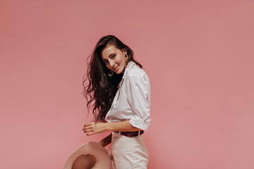 Wavy haired modern girl in gold earrings, light shirt and cool pants looking into camera, smiling...