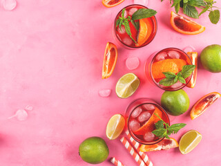 Refreshing summer red cocktail in glasses with blood orange and lime on pink background with mint