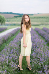 Beautiful young woman full length portrait in lavender field. Attractive girl with long healthy hair style enjoying walk outdoors in flowering lavender field