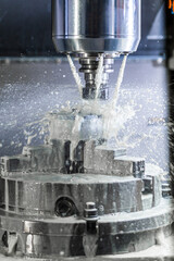 Vertical photo of industrial wet milling process in 5-axis cnc machine with coolant flow under...