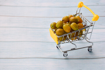 Gooseberries are stacked in a small toy yellow shopping cart. On the left side there is an empty...