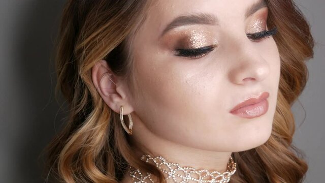 Portrait of beautiful young girl model in stylish evening make up smoky eyes posing. Long eyelash extensions eye makeup in delicate beige tones transparent lip gloss and necklace of rhinestones