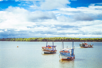 Three fishing boats in the sea with the shore in the background, trees and clouds in the blue sky. Cananéia, São Paulo, Brazil.