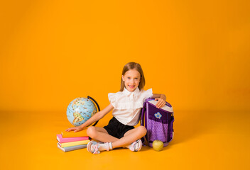 happy blonde schoolgirl in uniform is sitting on with school supplies on a yellow background with a...