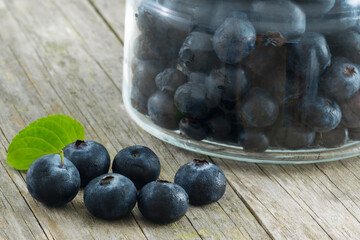 Blueberries over a wooden table with a mint leaf and a jar full of blueberries