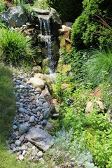 A man made waterfall and stream leading to a Koi fish pond on a sunny day