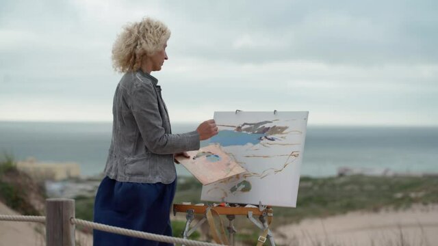 Middle-aged European woman, artist, paints a seascape with an original view of the sea. Slow motion
