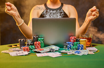 A young woman in a smart dress makes online bets on a sports game. In front of the woman is a laptop, and cards and chips are laid out. The risk, the hope of winning, the chance to win money.