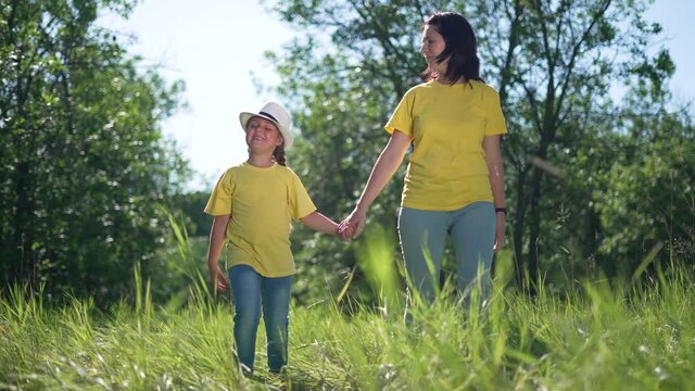 Happy family. Mom and daughter in forest park. People walk on grass. Happy team mom and daughter. Family is walk on grass in park. People walk along the tava in forest. Happy family concept