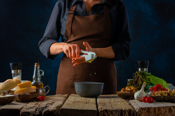 A festive dish of restaurant and home cuisine - Caesar salad. Cooking process. The chef squeezes out the garlic with a hand press for salad dressing. Dark blue background. Lots of bright ingredients.