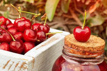 Wood box full of Cherries beside a jam jar with cork cap and a cherry over it with blurred background with negative space