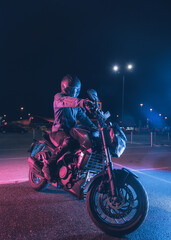 Fototapeta na wymiar Motorcyclist sits on a motorbike in neon light in an empty parking lot at night