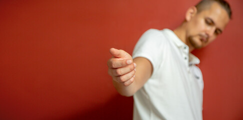 young guy on the background of a red wall with an outstretched hand on the camera.