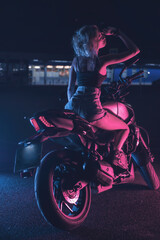 Plakat portrait of a girl in the rays of neon light on a motorbike at night in an empty parking lot