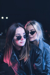 a couple of girls in love on a motorbike in the rays of neon light in an empty parking lot at night