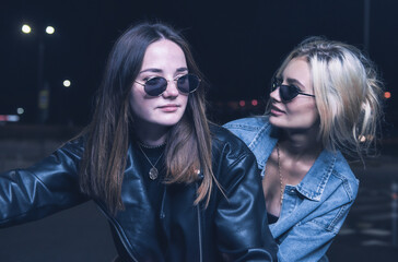 a couple of girls in love on a motorbike in the rays of neon light in an empty parking lot at night