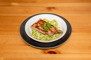 Green noodles sautéed in olive oil with a beef fillet on a white bowl and a black plate cooked by a Peruvian chef