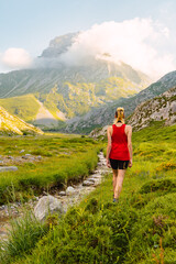 Caucasian young woman hiker walking along a small river with mountains in the background on a sunny day at sunset. weekend getaway and adventure.