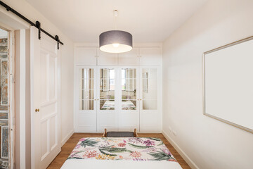 Bedroom with patterned bedspread, white wardrobe with mirrors and armchair