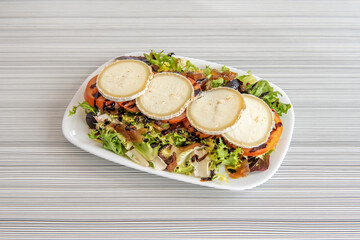 Sliced goat roll salad, caramelized onion, sliced tomato, lettuce and endive with drops of Modena balsamic vinegar