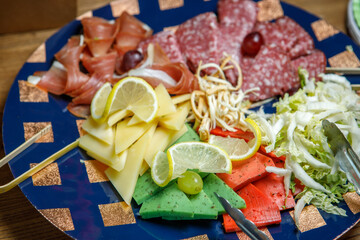 Assorted cheese, sliced sausage, grapes, lemon and herbs on a plate.