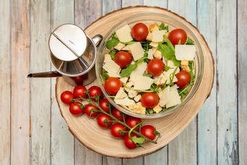 Glass bowl with Italian arugula salad, Parmesan cheese slices, cherry tomatoes inside and outside the bowl, arugula base and croutons with Spanish olive oil in stainless steel oil can