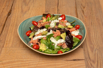 Super montage of smoked salmon salad with dill sprinkles, hand chopped fresh cheese, lettuce shoots, spinach and arugula, olive oil and cheerful pear tomatoes on a wooden table