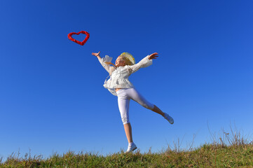 A young girl dressed in white, throws a red
heart up high in the air. The young girl has
an expression of happiness on her face.
