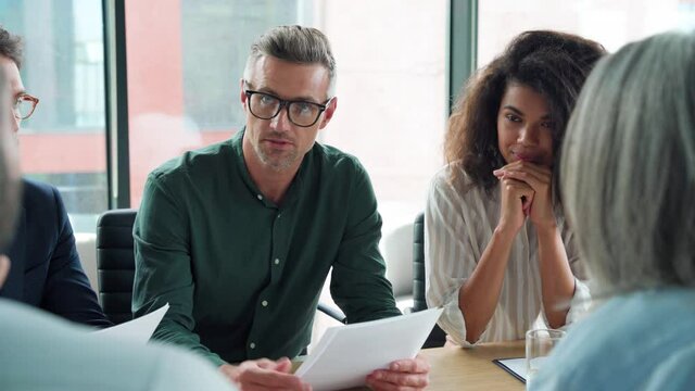 Business man discussing financial contract at executive team meeting. Diverse international business people group negotiating on partnership agreement plan at boardroom table doing paperwork in office