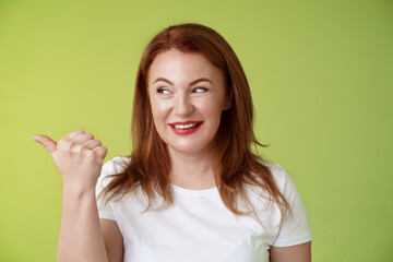 Intrigued charismatic redhead middle-aged woman smiling temtation interest pointing looking left...