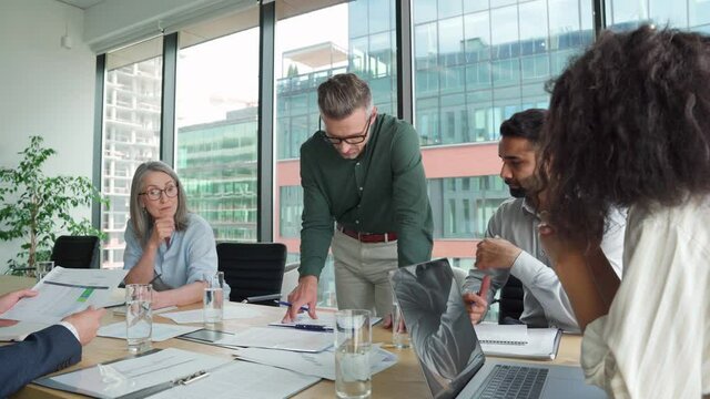 Executive team business people listening to ceo negotiating discussing project results at board meeting. Multicultural professional company leaders working sitting at boardroom table in office.