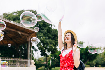Joyful young hispanic woman having fun while playing with soap bubbles in city park - Smiling...