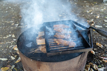 Marinated chicken breasts cooking over a campfire ring. Lots of smoke from the campfire. Selective...