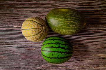 Fototapeta na wymiar Two melons and a watermelon viewed from the top. Small green seedless watermelon, toad skin melon and small galia melon on wooden log.