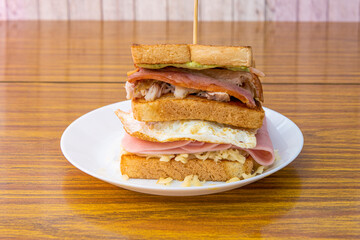 Super two-story sandwich with cheese, green sauce, fried bacon, shredded chicken, ham and fried egg with grilled sliced bread