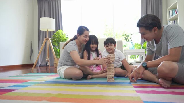 Asian family parents with little daughter and son sit on the floor playing wooden toy together with happiness. Father and mother with child boy and girl having fun weekend activity lifestyle at home.