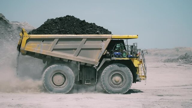 A dump truck loaded with ore drives through a dusty open pit mine.