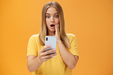 Waist-up shot of shocked and stunned emotive young woman reacting to shocking terrible news reading...