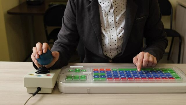 An unrecognizable woman with cerebral palsy is typing on the keyboard. A girl with disabilities works on a specially equipped computer