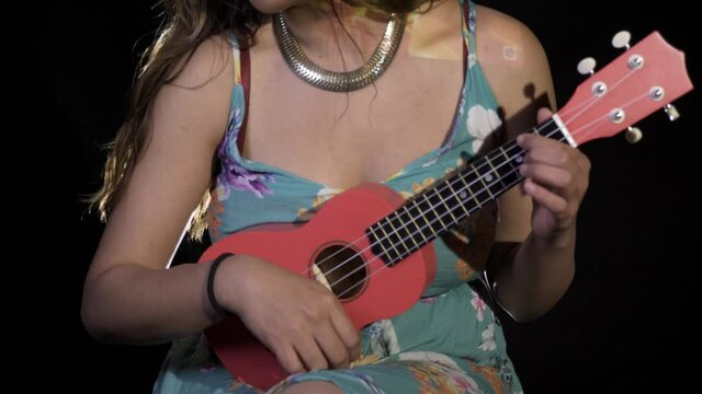 An adult Hispanic woman playing the ukulele while filming a music video with visual effects in 4K
